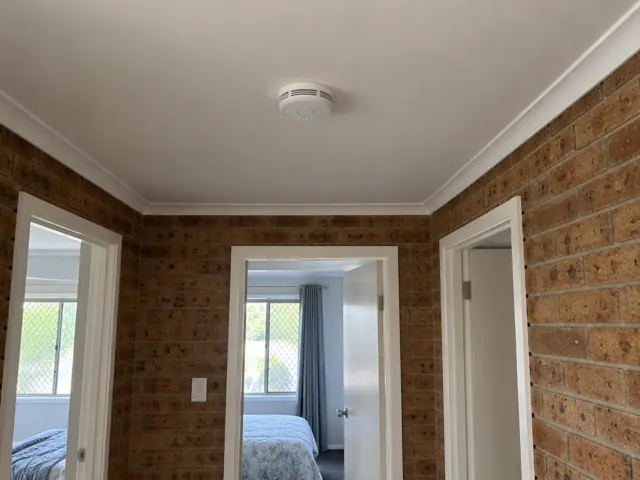 Ceiling smoke alarm in a brick-lined hallway with white door frames in Miami